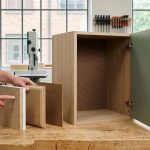 Майстер у майстерні демонструє зразки ДСП, МДФ та ДВП поруч із розпашною шафою.